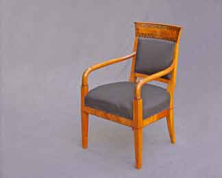 Das Bild zeigt ein Biedermeier-Möbel nämlich einen Armlehnsessel aus Kirschbaumholz mit Schwarzlotmalerei auf der Rückenlehne
