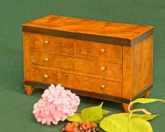 Das Bild zeigt ein kleines Biedermeier-Möbel. Es ist eine Biedermeier-Modellkommode in Kirschbaum mit teils schwarzen Kanten und auf der Front durchlaufender Maserung.