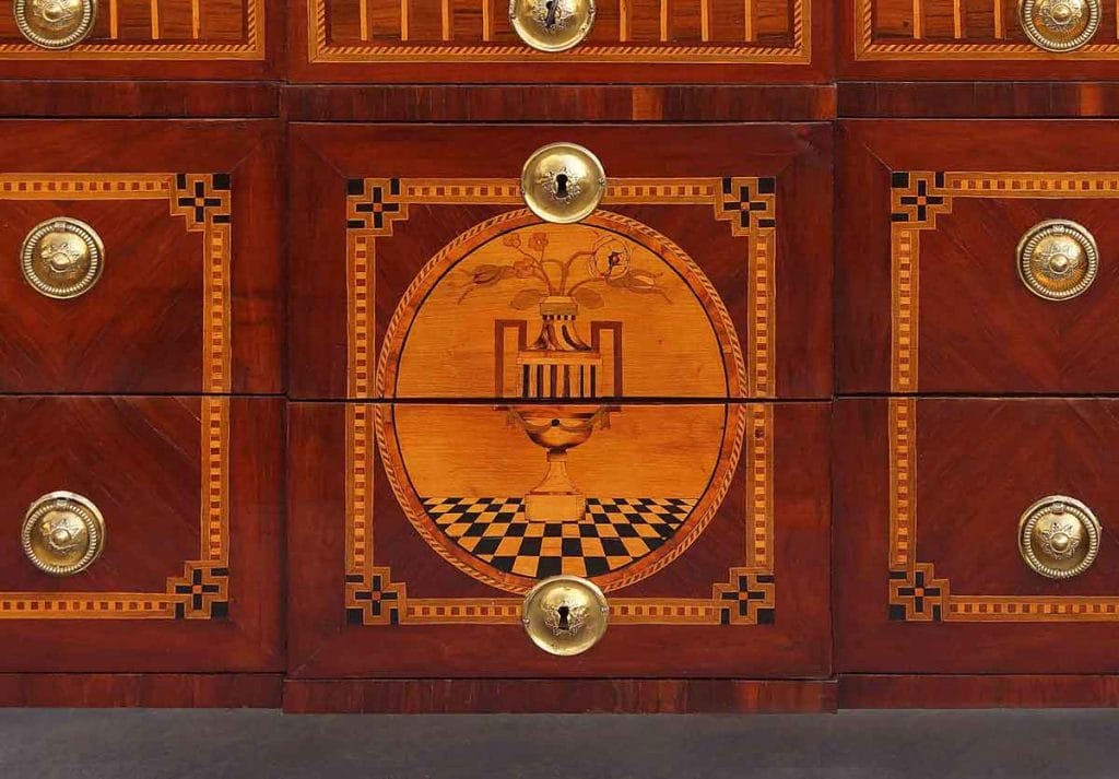 Louis XVI Kommode Intarsien Kommode mit einem über zwei Schubladen gehenden Intarsie. Es wird eine Vase auf einem schwarz weißen Parkett dargestellt aus dem Blumen wachsen.