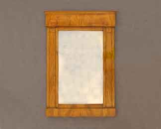 Auf dem Foto ist ein Biedermeier-Spiegel zu sehen. Er ist südwestdeutsch und aus Nussbaumholz gefertigt.
