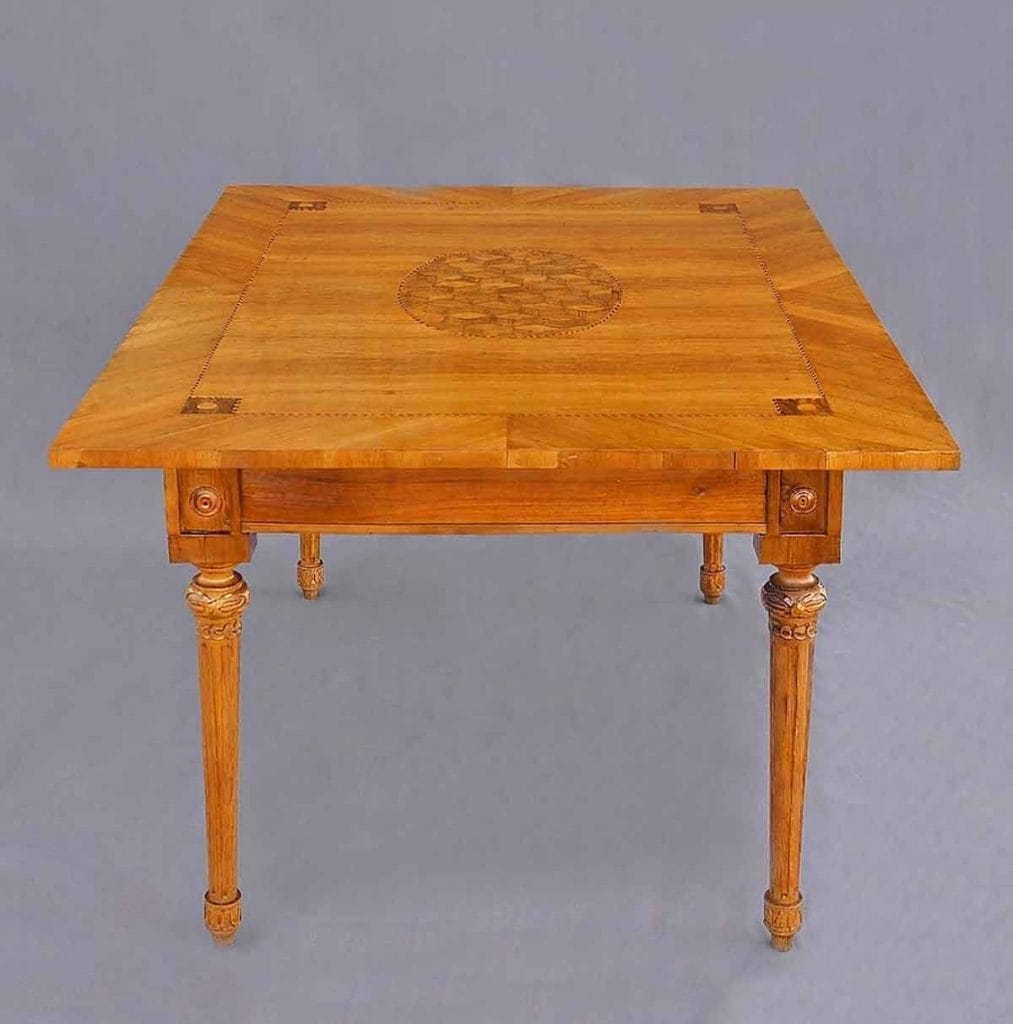 Louis Seize Tischplatte4 Auf die schmale Seite eines Tisches gesehen: Ein antiker Louis-seize-Tisch aus Kirschbaumholz mit kunstvollen Marketerie-Einlagen auf der Tischplatte und kannelierten, spitz zulaufenden Beinen.