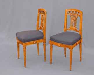 in Paar antike, geschnitzte Holzstühle im Louis-seize-Stil mit hellbraunem Gestell, dunklen Sitzpolstern und kannelierten Beinen vor einem neutralen grauen Hintergrund.