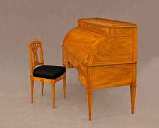 Frontansicht eines klassischen, geschlossenen, herrschaftlichem Zylinderbureaus aus poliertem, warmtönig gemasertem Nussbaumholz. Das antike Möbelstück steht vor einem neutralen, grauen Stoffhintergrund und verfügt über drei kleine Schubladen im Aufsatz sowie vier weitere Schubladen im unteren Bereich, alle mit runden Messingbeschlägen. Der Schreibtisch wird von vier eleganten, konisch zulaufenden Beinen getragen.