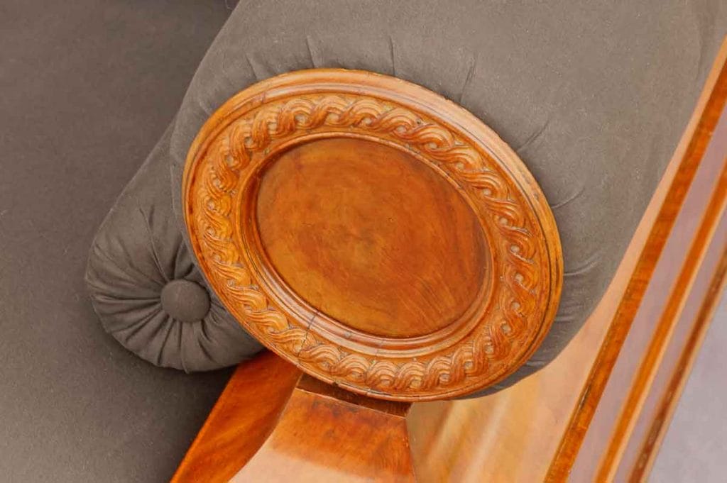 Biedermeier Sofa Nordeutsch Detail2 Nahaufnahme der runden, dekorativen Holzscheibe mit geschnitztem Wellenrand an der vorderen Seite der zylinderförmigen Armlehne des Biedermeier-Sofas.