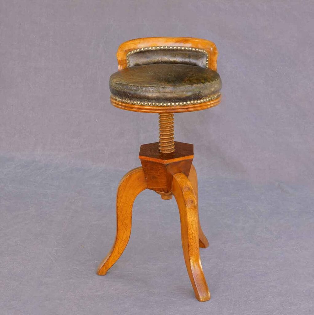 Biedermeier-Klavierhocker Hochgedrehter Biedermeier-Drehhocker aus Holz mit Lederpolsterung, sichtbarer Gewindespindel und drei geschwungenen Beinen.