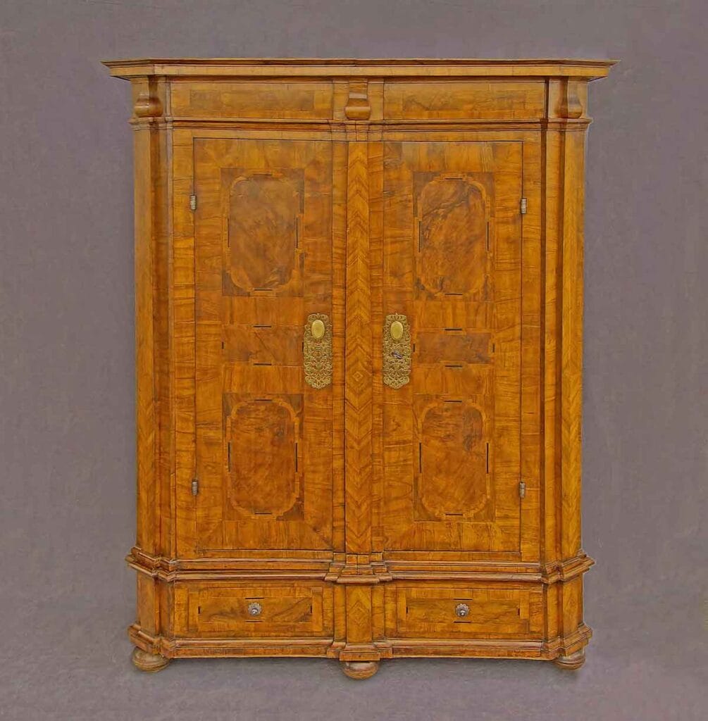 Barock-Schrank2 Frontansicht eines zweitürigen Barockschranks aus edlem Holz mit meisterhaften Intarsien, Messingbeschlägen und zwei unteren Schubladen vor grauem Hintergrund.