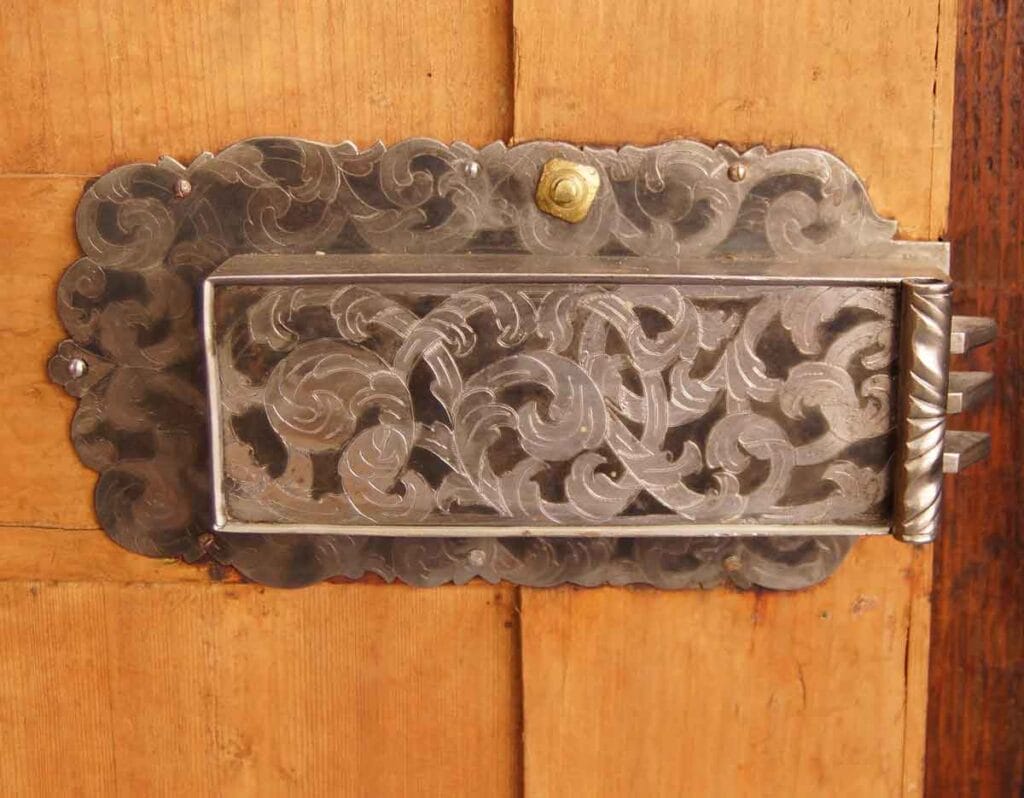 Barock-Schrank7 Detailaufnahme eines antiken, floral gravierten Kastenschlosses aus Eisen an der Innenseite einer hölzernen Schranktür.