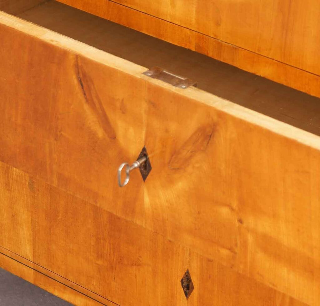 Biedermeier-Kommode-Kirsch3 Detailansicht einer geöffneten Kirschbaumholz-Schublade der Kommode mit steckendem Metallschlüssel im rautenförmigen Schlüsselschild