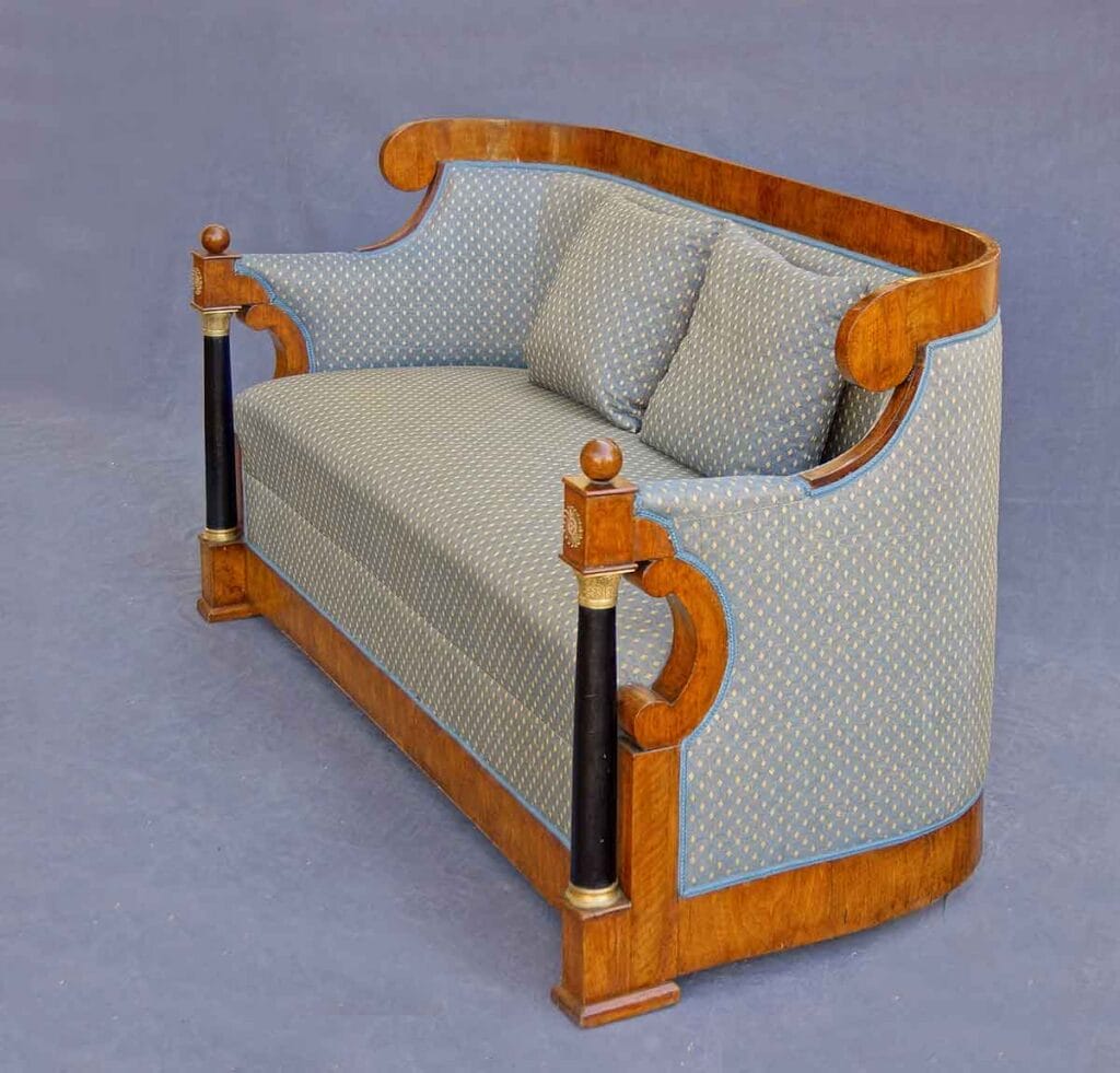 Biedermeier-Sofa1 Biedermeier-Sofa aus Holz in schräger Seitenansicht mit blauem Rautenstoff, zwei Kissen und verzierten schwarzen Frontsäulen.