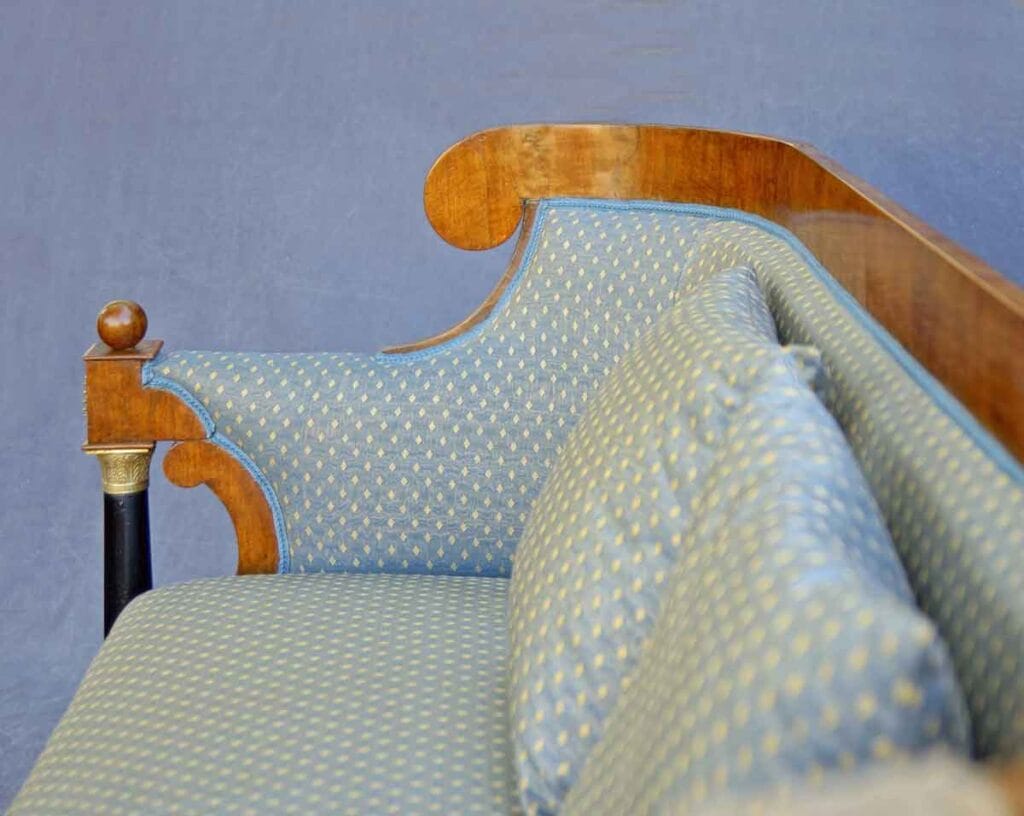 Biedermeier-Sofa4 Seitenansicht der linken Hälfte eines Biedermeier-Sofas mit geschwungener Armlehne, blau-goldenem Musterstoff und Rückenkissen.